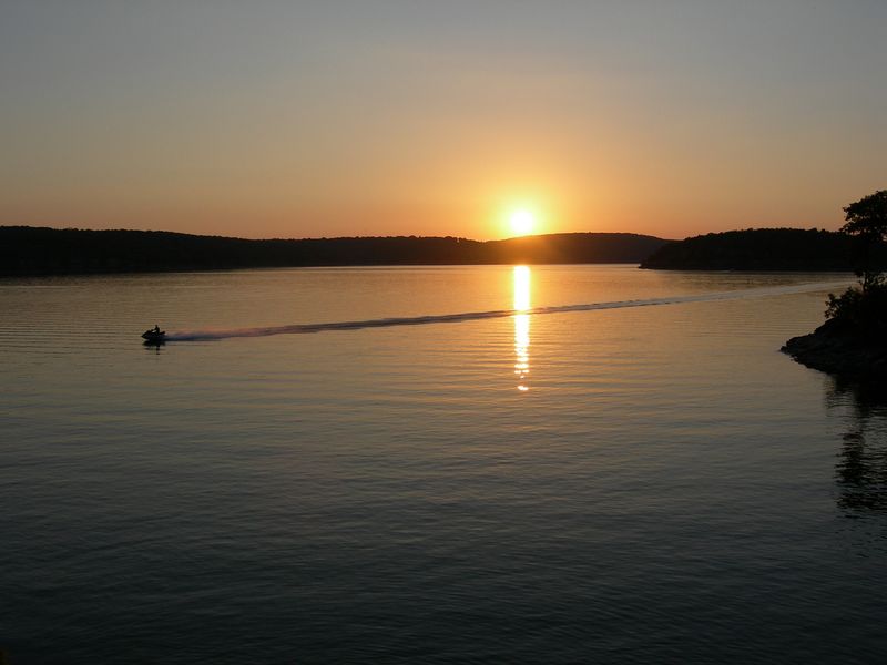 A lone jet skier flies across that surface of Lake Tenkiller, which is bathed in the golden hues of a gorgeous sunset.