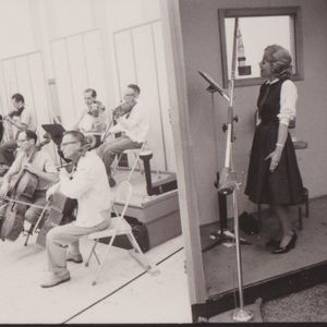 Patti Page sings along with the band in a recording studio booth.